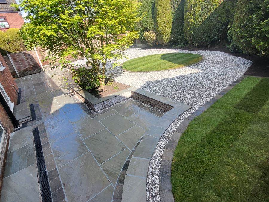 A sandstone terrace opening onto a lawn with a circular gravel feature