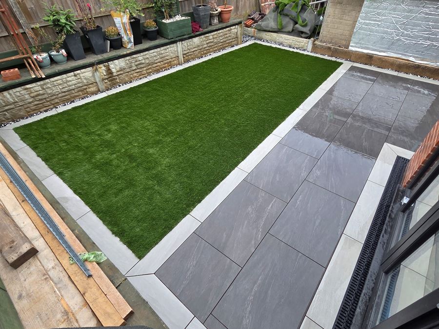 An artificial lawn edged by a grey porcelain terrace in an enclosed garden